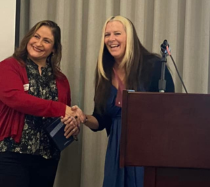 Katie Kelly standing at a podium shaking a NHCDD employee'd hand.