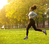 Woman jogging in an open field with fall foliage in the background.