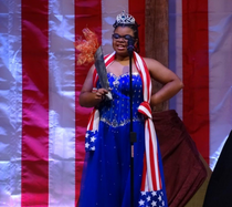 Woman in a sparkly blue dress wearing a tiara and caring a torch smiling. 