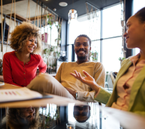 two women and a male coworker sitting at a table discussing work over coffee.