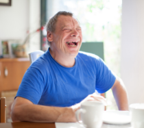 Man laughing while sitting at a table wearing a blue shirt.