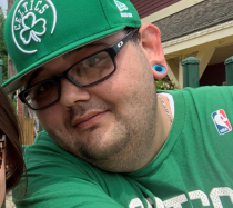 Shane smiling for a photo wearing a green Celtics hat.